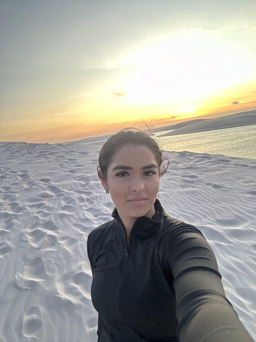 Bianca taking a selfie on the white dunes of Lençóis Maranhenses, with the sunset and a lagoon behind her